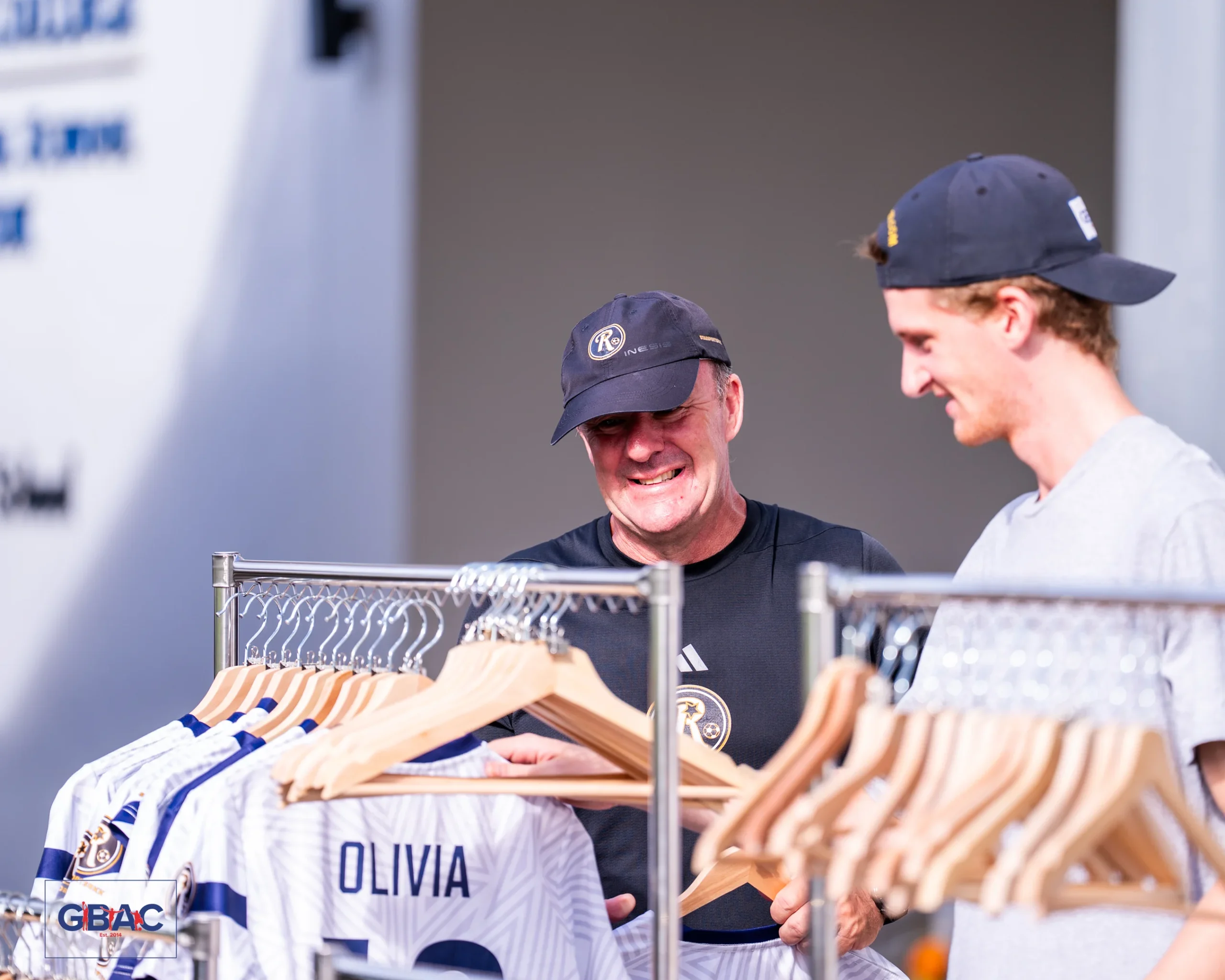 Two men smiling while browsing GBAC event shirts at the Star Sports BKK merchandise stall