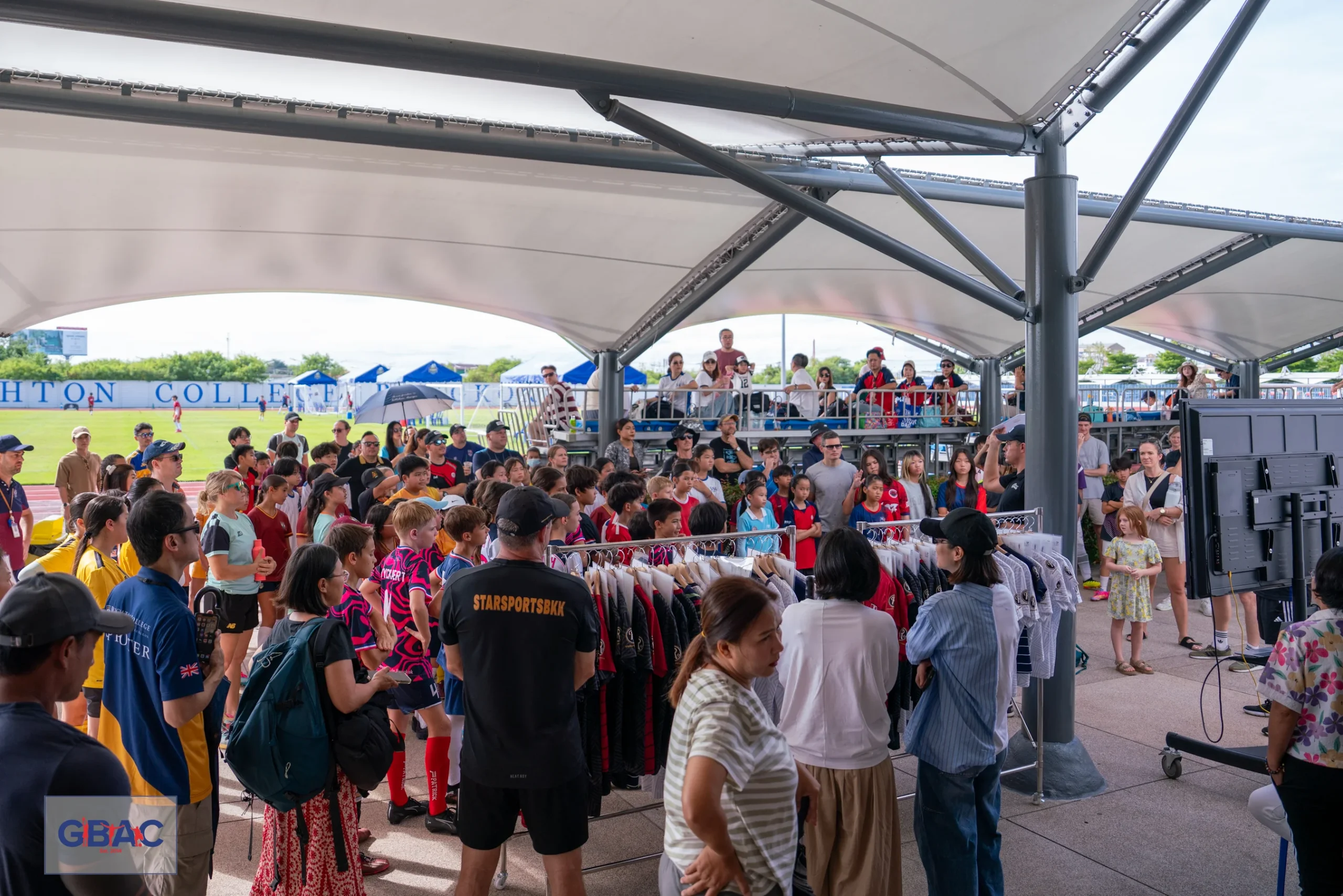 Large group of students and parents gathered under a tent at the GBAC event merchandise area