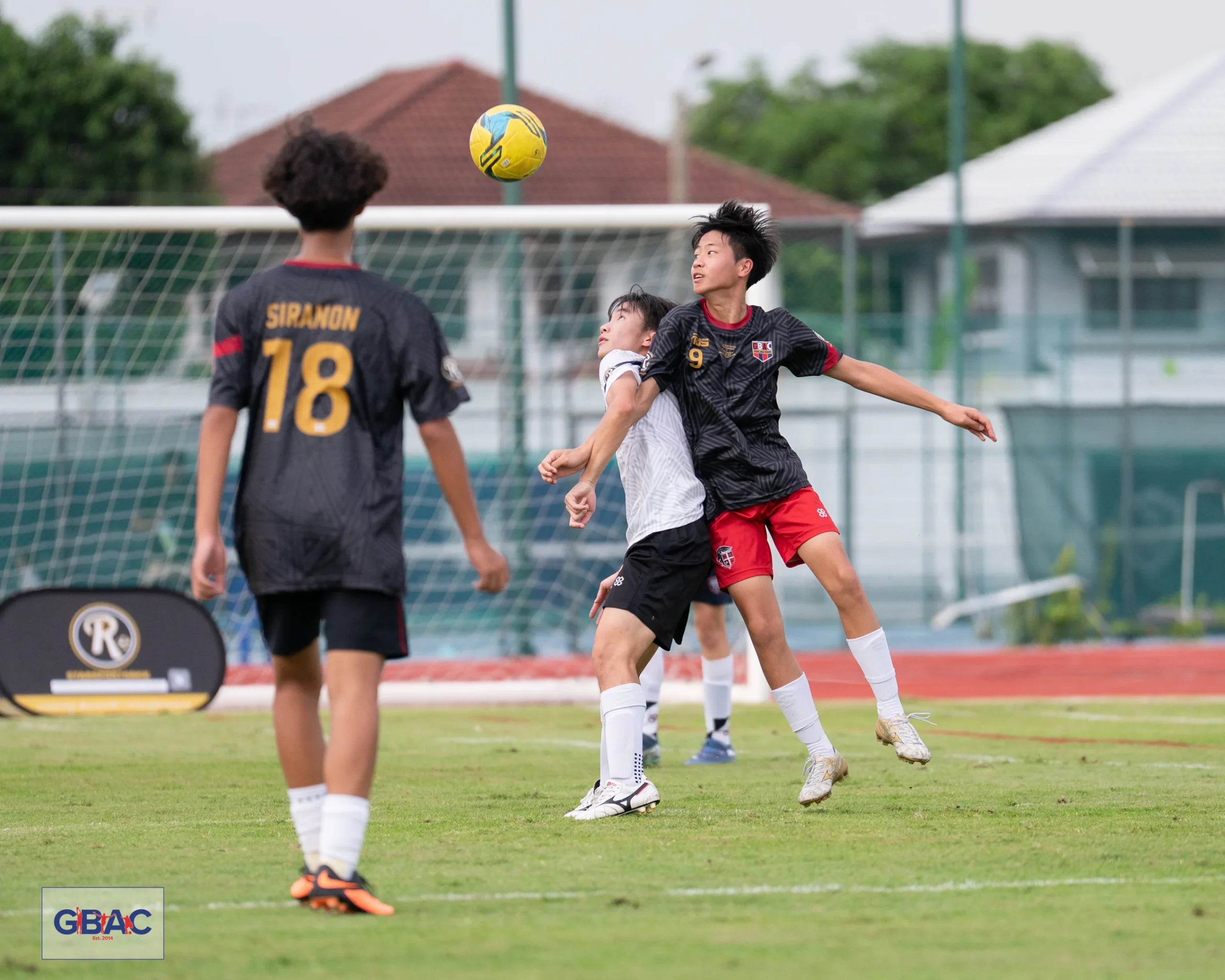 Two players leap into the air to head the ball during a competitive moment at a GBAC football match