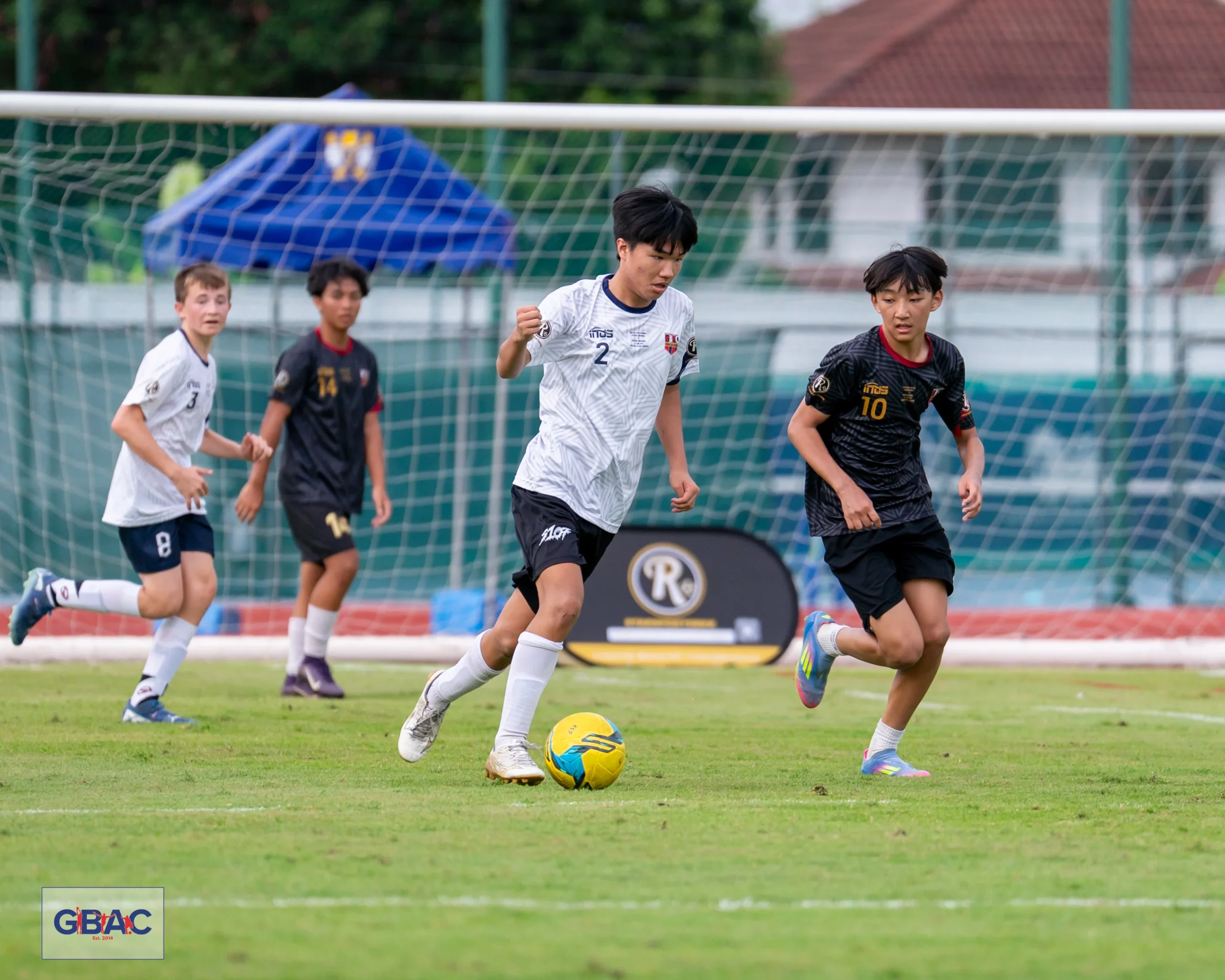 Young players chase the ball during a GBAC football match, with intense focus on the field